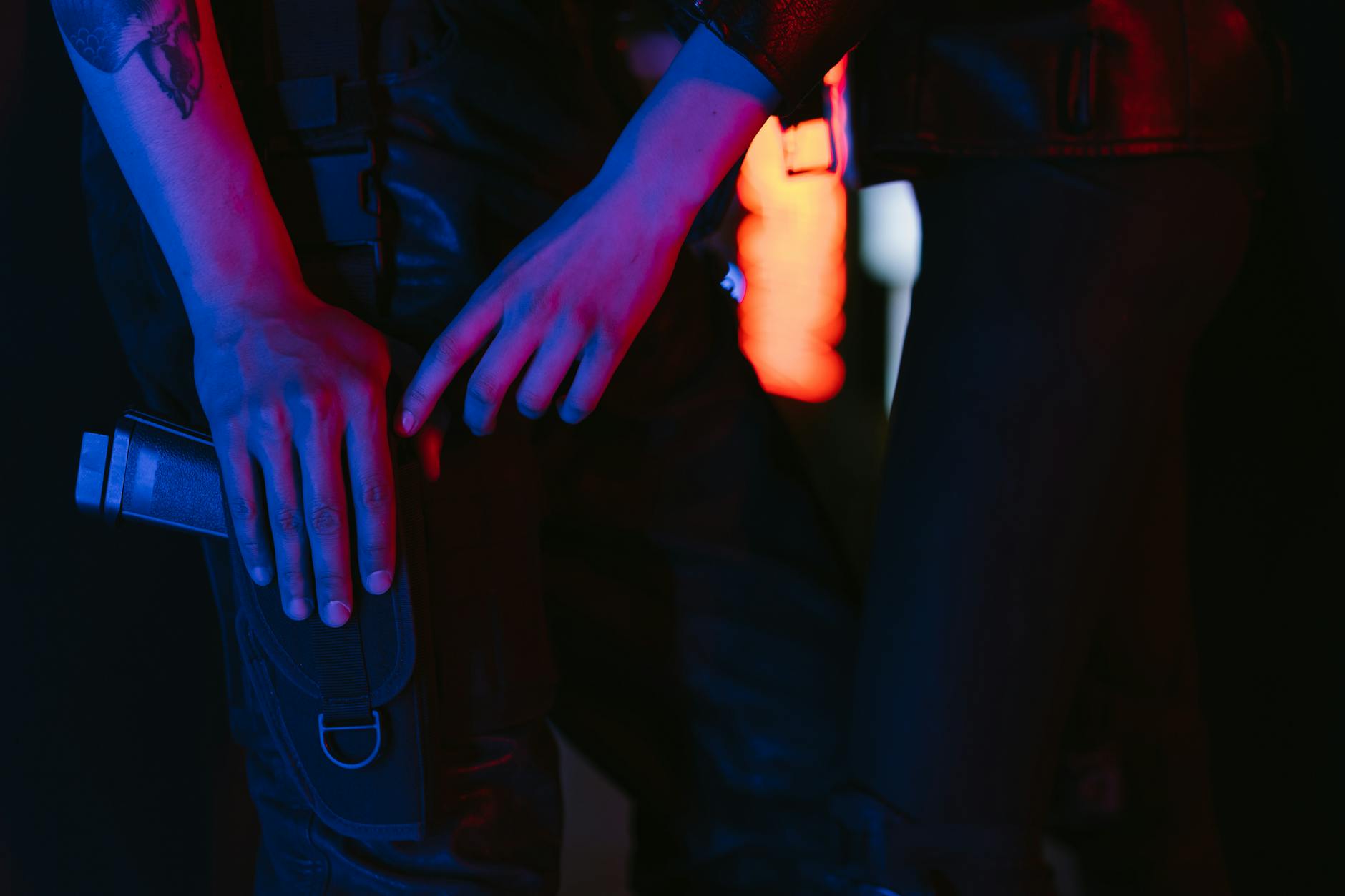 Close-up of a person in cyberpunk attire holding a futuristic weapon, illuminated by neon lights.