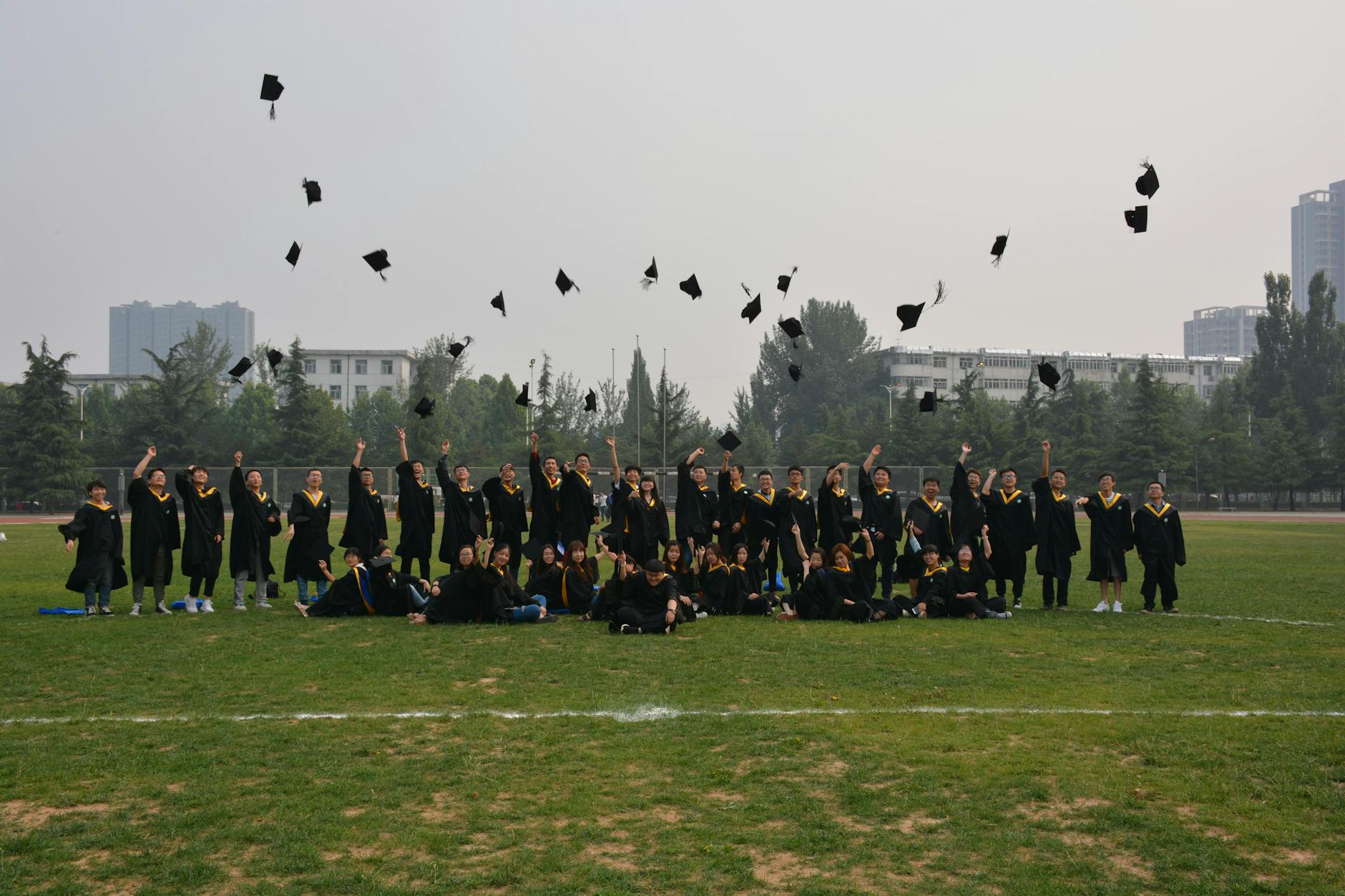 A large group of graduates celebrating by tossing their caps in the air outdoors.
