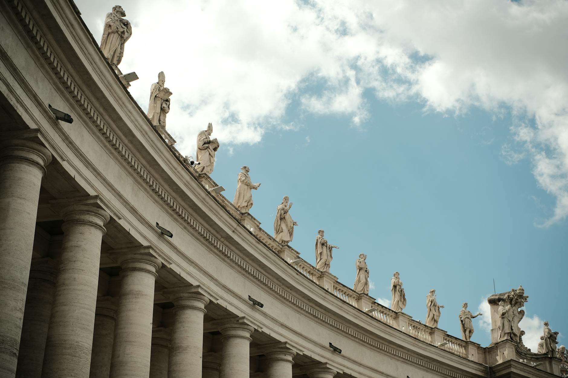 A low-angle view of statues atop columns at St. Peter's Square, Vatican City.