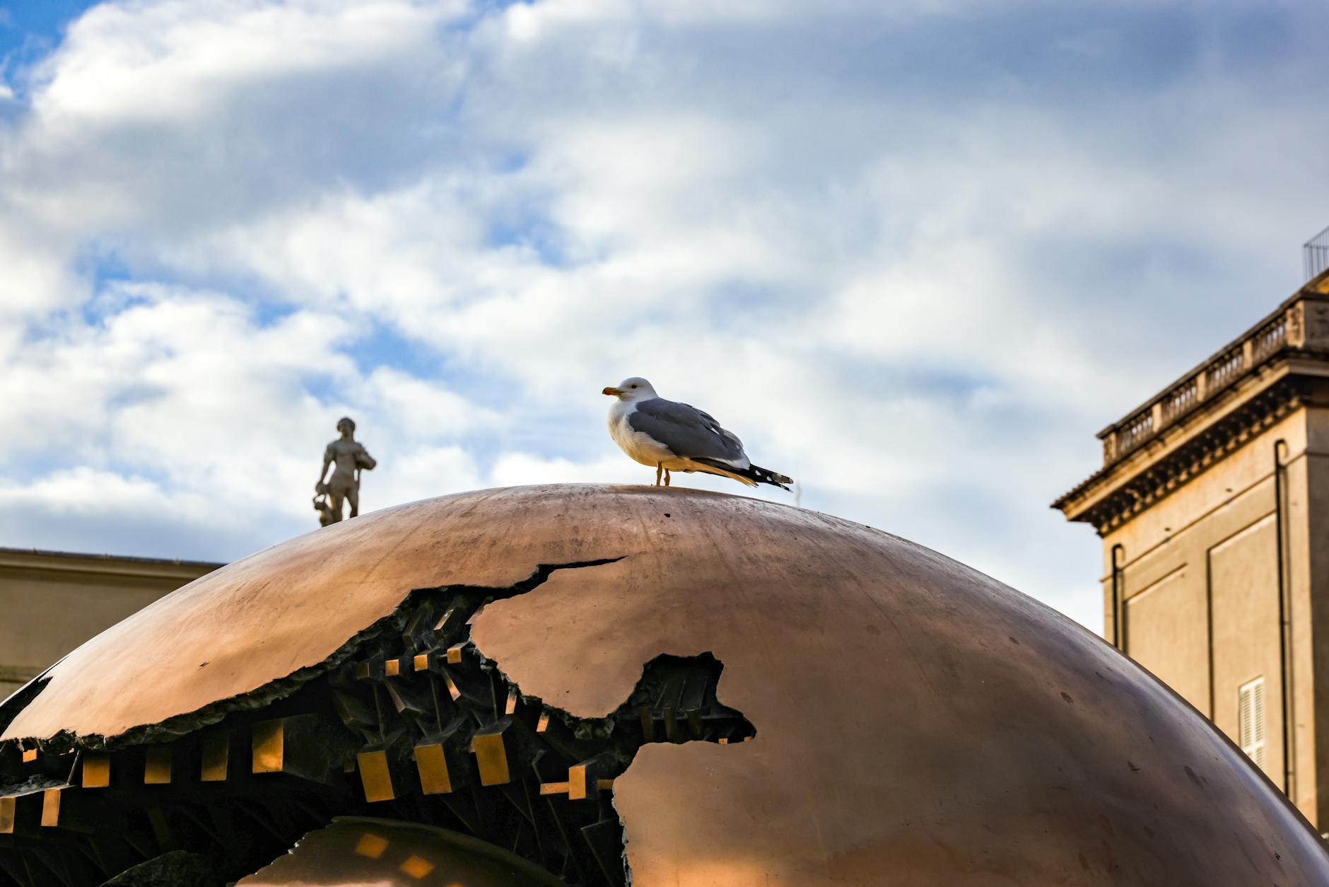 A seagull perched on the Sphere Within Sphere sculpture in Vatican City, showcasing iconic art and architecture.