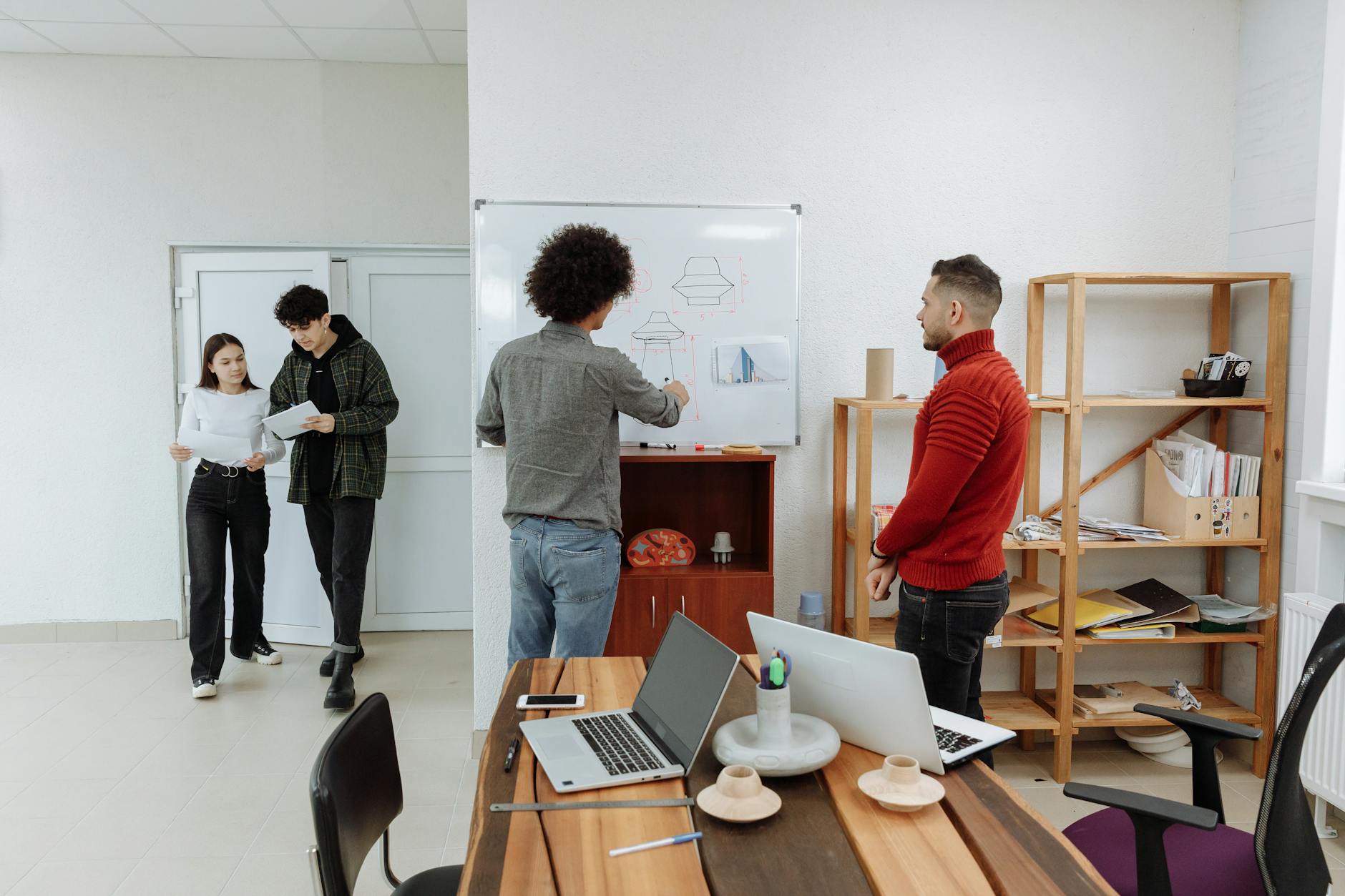 Diverse team collaborating in a modern office, discussing ideas with laptops and a whiteboard.