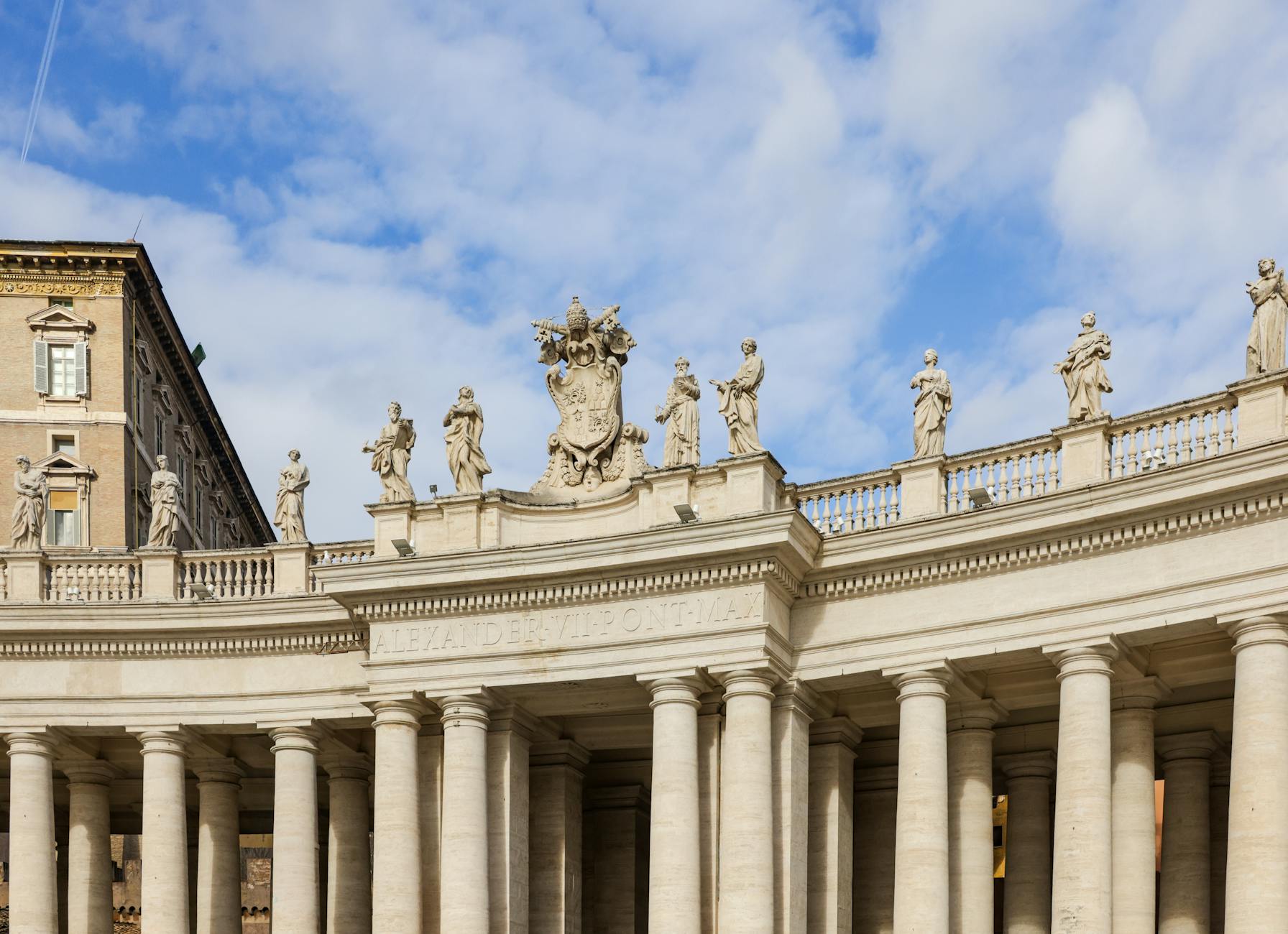 Historic colonnade and statues at St. Peter's Square under a blue sky, Vatican City.