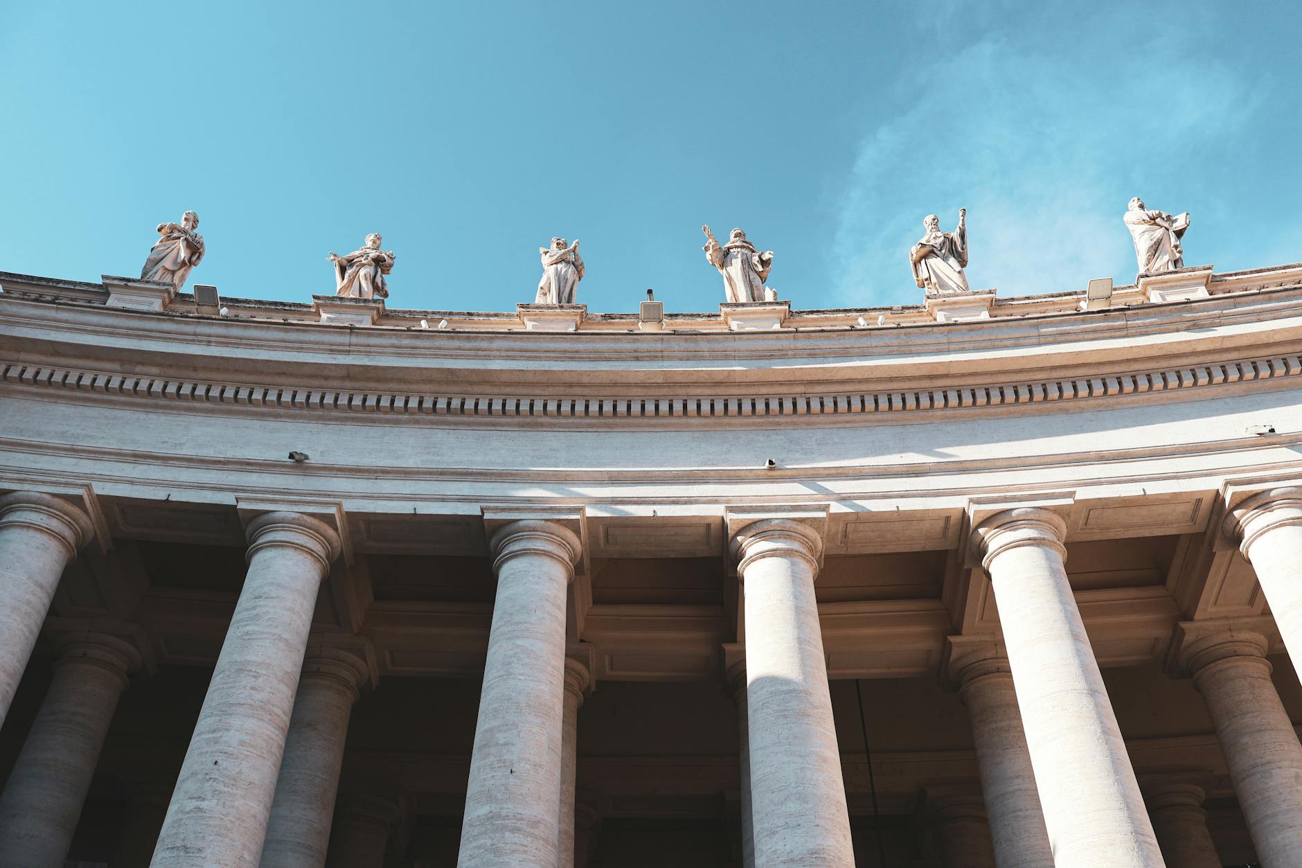 Majestic view of arched architectural columns with statues in Vatican City, under a clear blue sky.