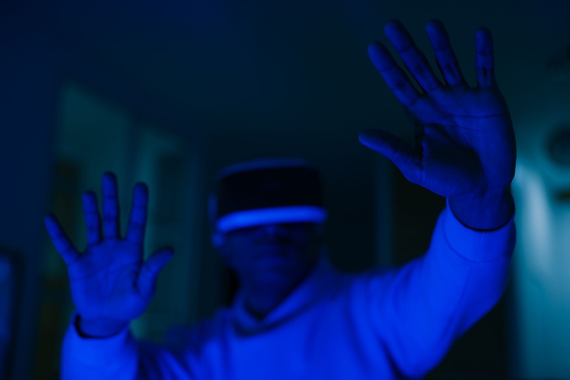 Man wearing VR headset immersed in virtual reality with visible hands in blue lighting.