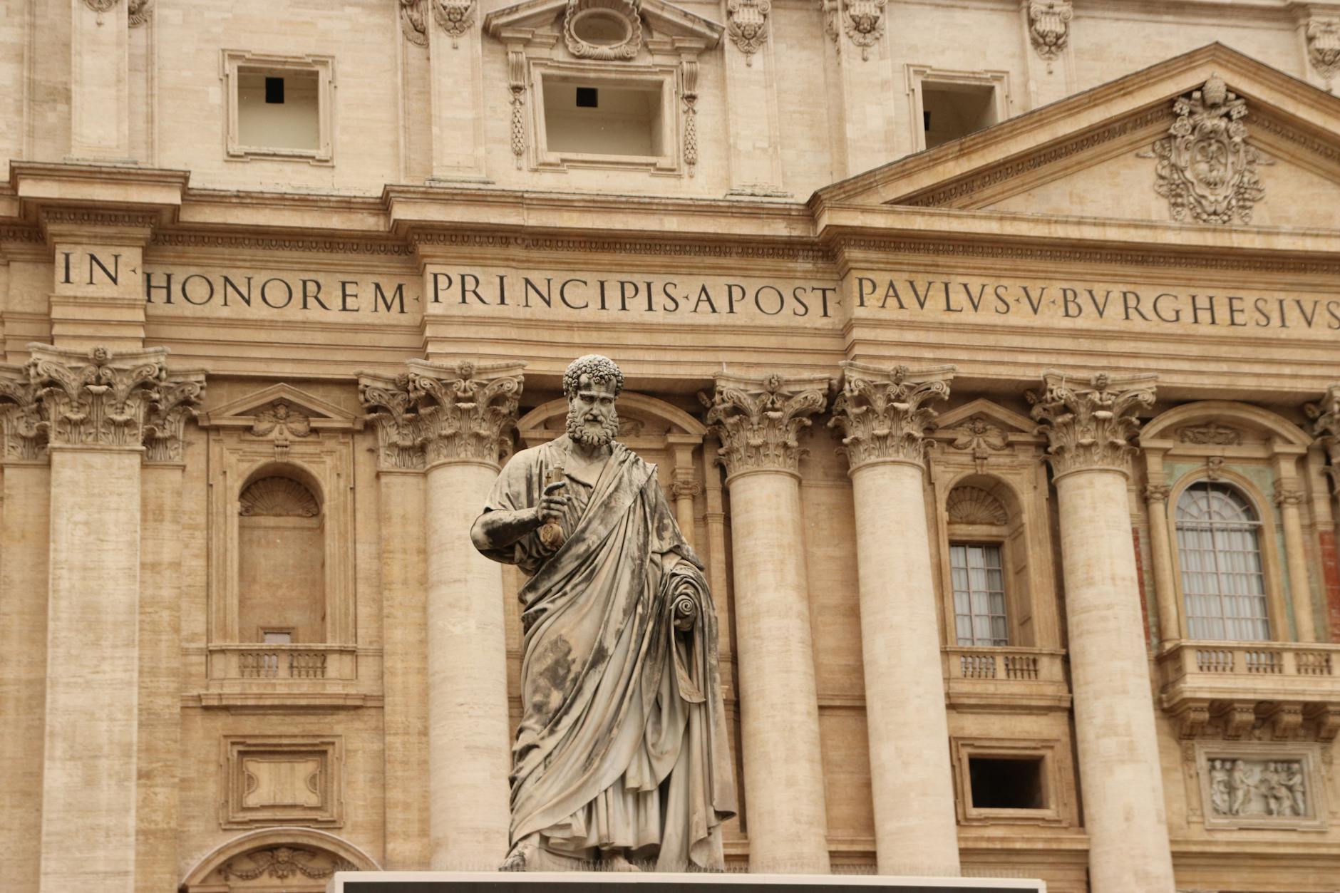St. Peter statue in front of St. Peter's Basilica facade in Vatican City, showcasing classic architecture.