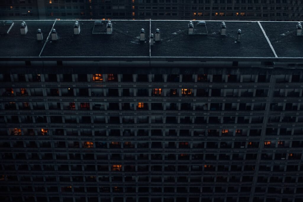 Aerial view of massive futuristic data center at dusk with glowing server rows, construction cranes expanding infrastructure, ambient blue and orange lighting, professional tech atmosphere