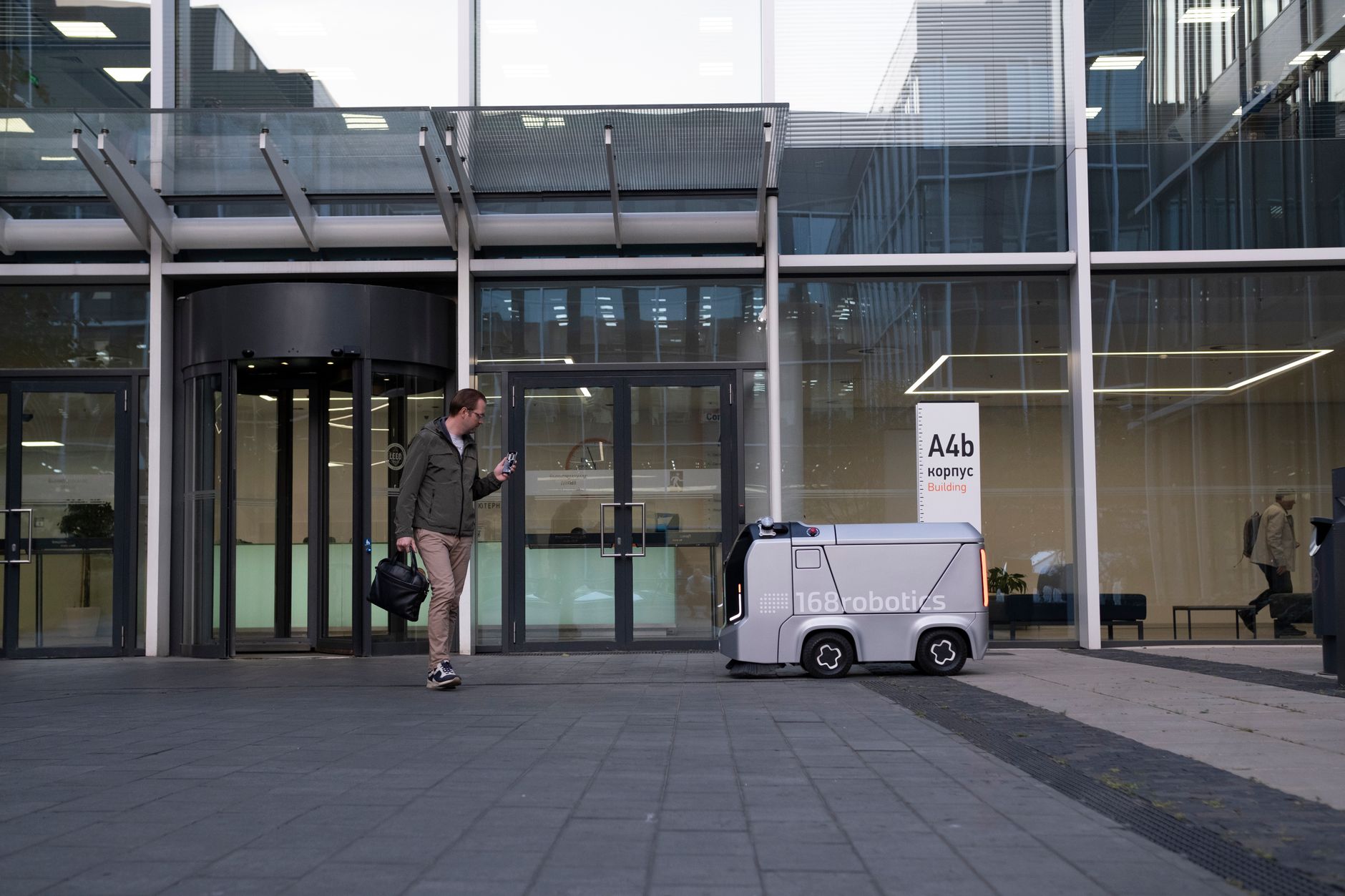 A man encounters a delivery robot outside a modern glass building.