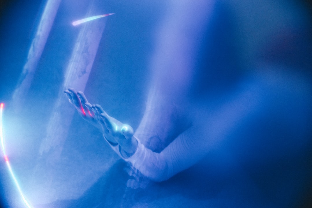 Aerial view of human and robotic hands reaching toward glowing microchip on reflective surface, sunrise through futuristic data center windows, warm golden ambient light mixing with cool blue server i