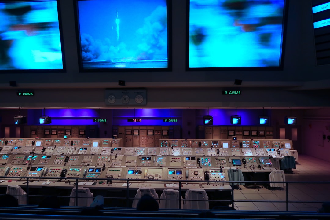 Futuristic military command center with holographic battlefield displays, blue ambient lighting, uniformed officers analyzing AI data streams, sleek glass consoles, dark moody atmosphere