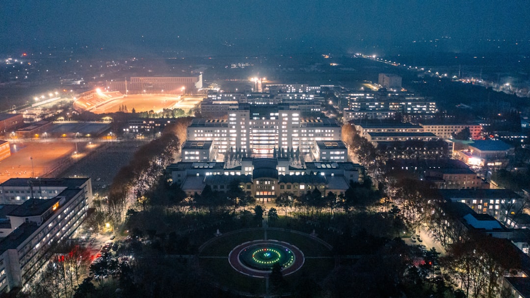 Futuristic university campus at twilight with holographic data displays showing enrollment analytics, diverse students studying outdoors, sleek modern architecture, ambient blue lighting, digital over