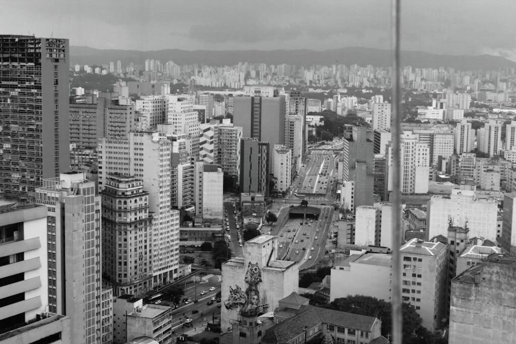 Aerial view of futuristic São Paulo cityscape at dusk with holographic satellite data overlays, sleek glass towers, ambient blue and green lighting, professional tech aesthetic, river visible below wi