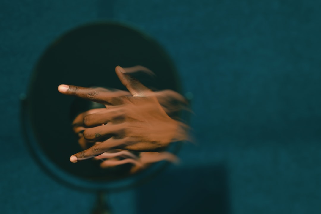 Human hand reaching toward cracked mirror reflecting robotic face, dark moody atmosphere, glitch art distortion, emotional isolation concept, neon accent lighting