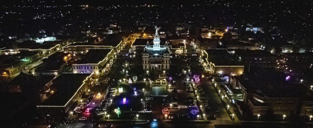 Aerial view of diverse state capitol buildings connected by glowing blue neural network lines, holographic data streams, dusk sky, futuristic policy visualization, clean editorial style