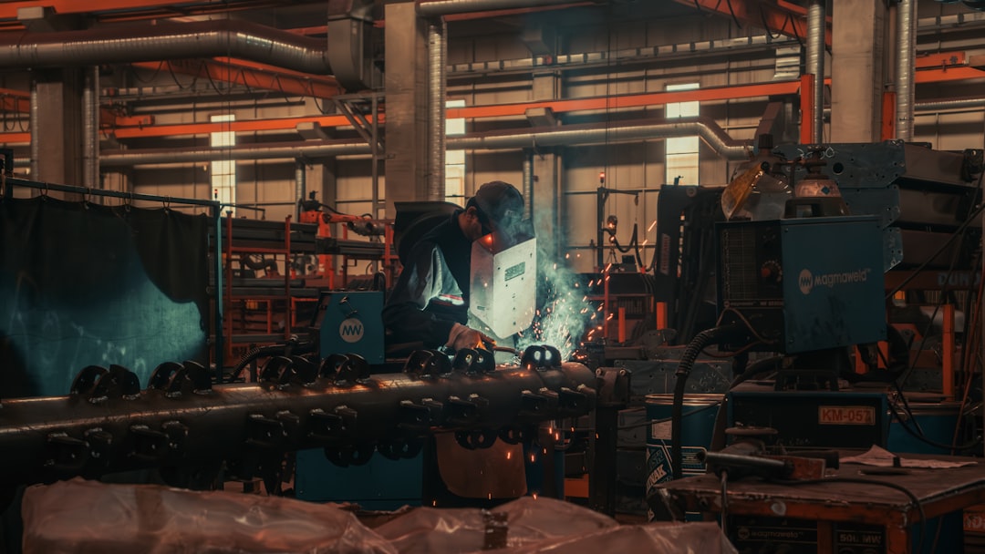 Industrial robotics arm assembling components with holographic overlay, clean modern factory floor, professional engineer monitoring, sleek ambient lighting, orange and teal color grading, digital tra