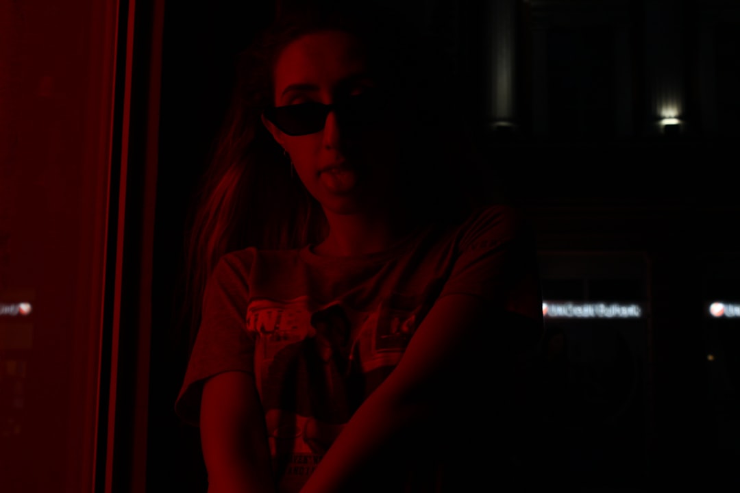 Glitching algorithmic code projected onto anxious professional woman's face in dark server room, red warning lights, cybersecurity dashboard reflections, crisis of trust mood, data center catastrophe 
