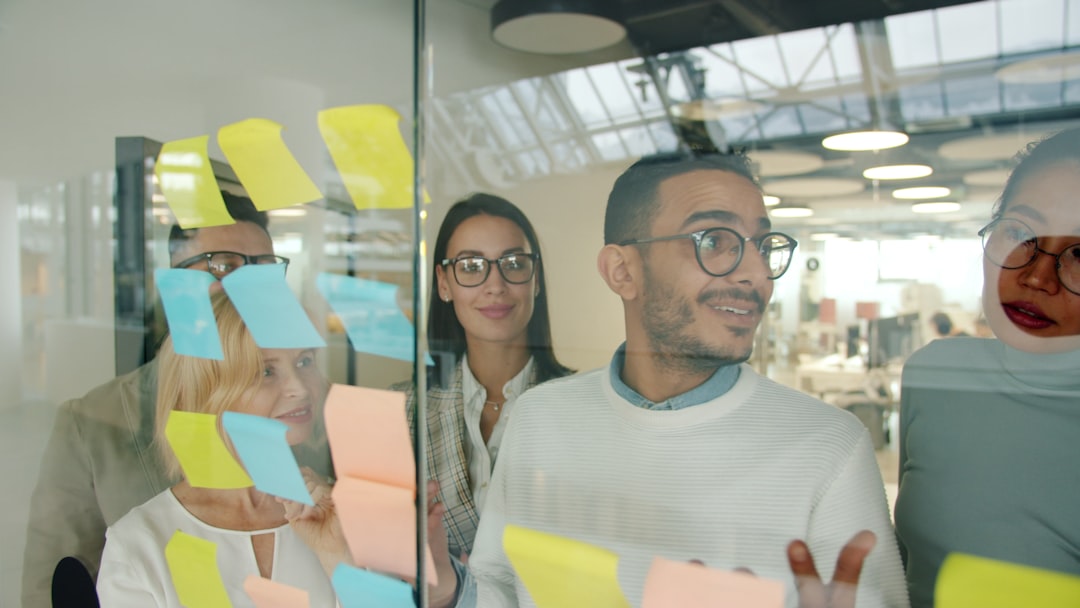 Diverse team of three creative professionals collaborating around futuristic transparent display, warm human-focused lighting contrasting with cool tech elements, emphasizing human connection and crea