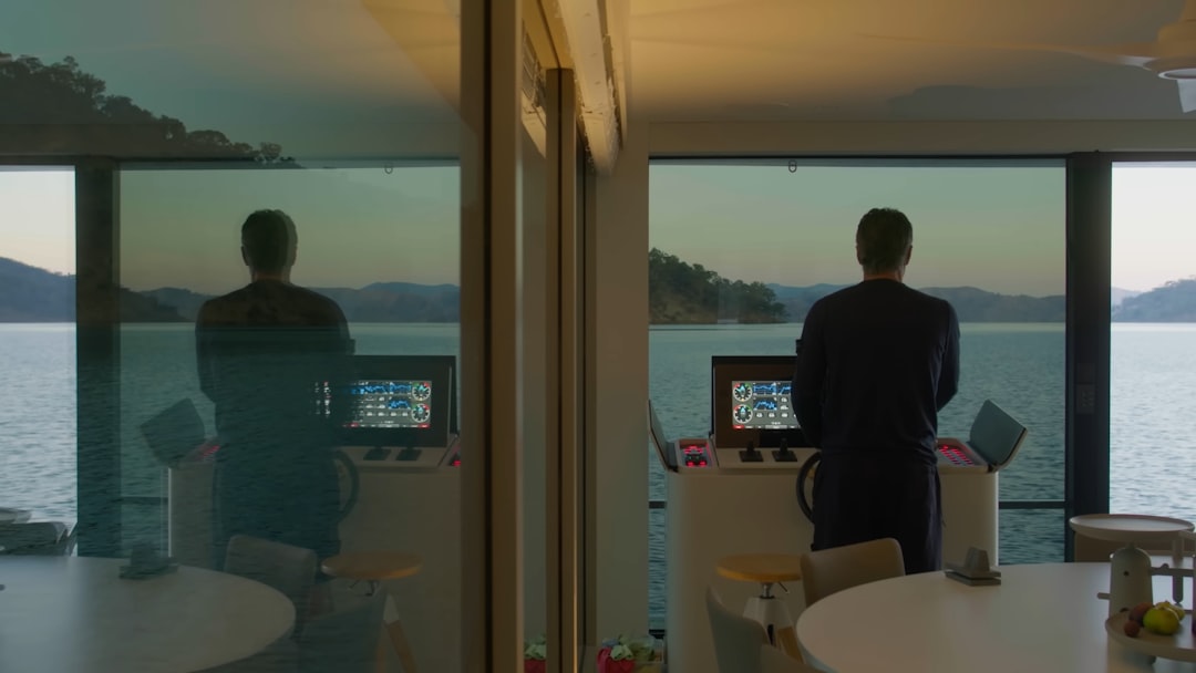 Clean modern office with two distinct holographic AI agent interfaces facing each other, human professional observing autonomous system dashboards, ambient warm and cool contrast lighting, futuristic