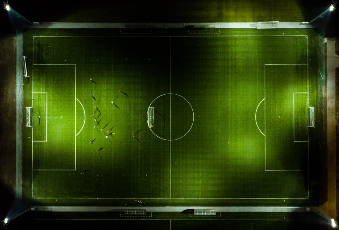 Professional soccer coach analyzing holographic tactical display with real-time data overlays in sleek dark control room, ambient blue lighting, futuristic sports technology interface, neural network