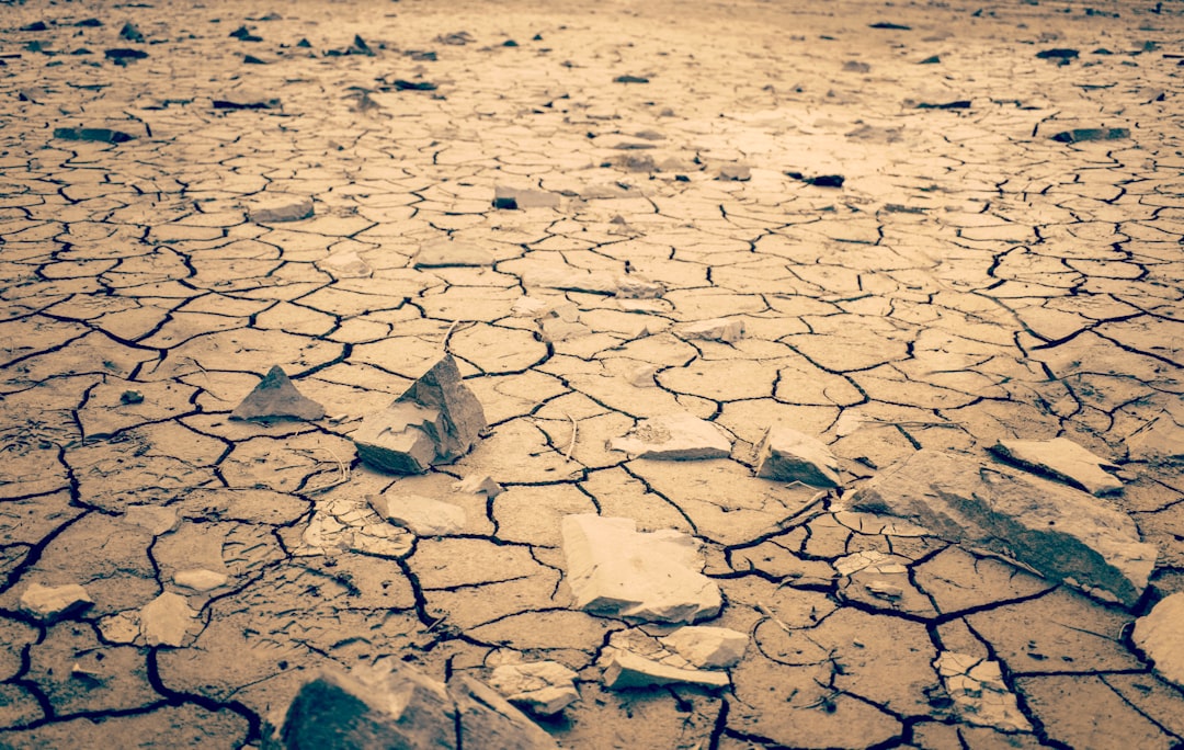 Dramatic aerial view of dried cracked earth meeting glitched digital grid overlay, warm amber and cold cyan lighting, climate collapse concept, neural network patterns dissolving into dust, cinematic 