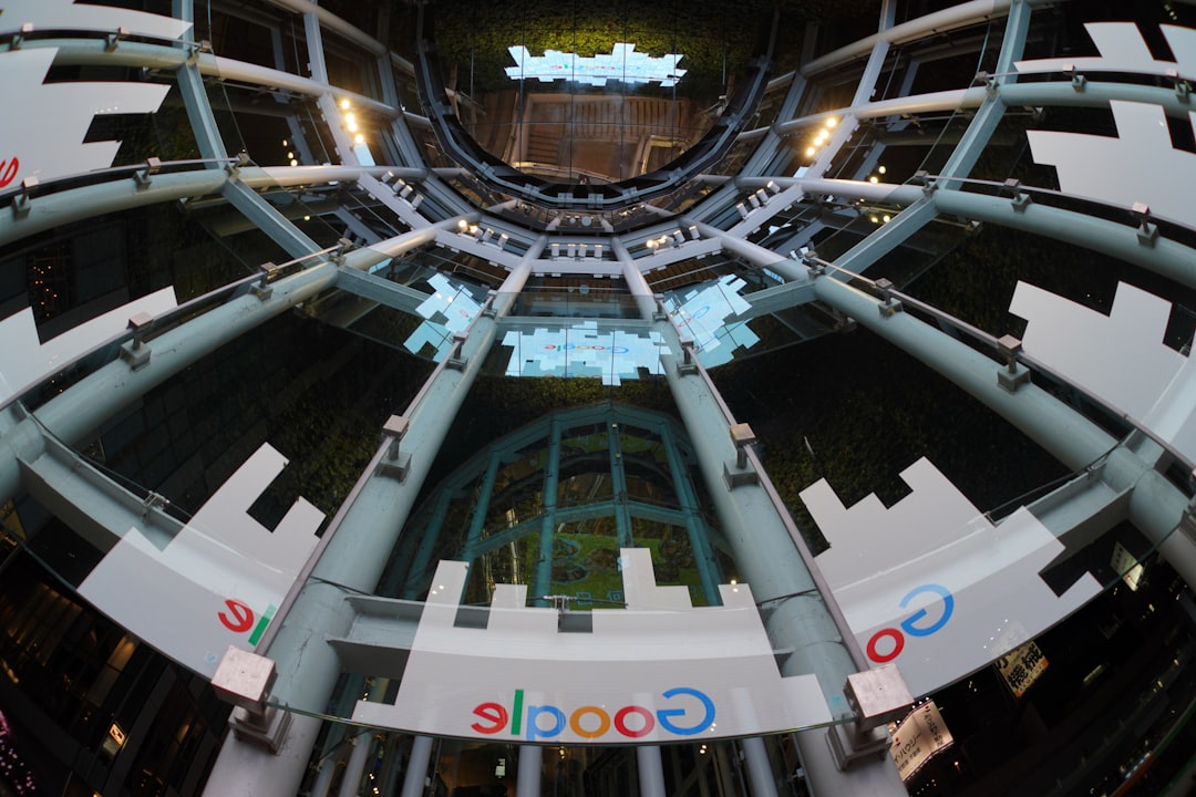 Google developer conference atmosphere with massive curved holographic display showing consumer AI roadmap, diverse professionals engaging with transparent interface, ambient purple-blue lighting, sle
