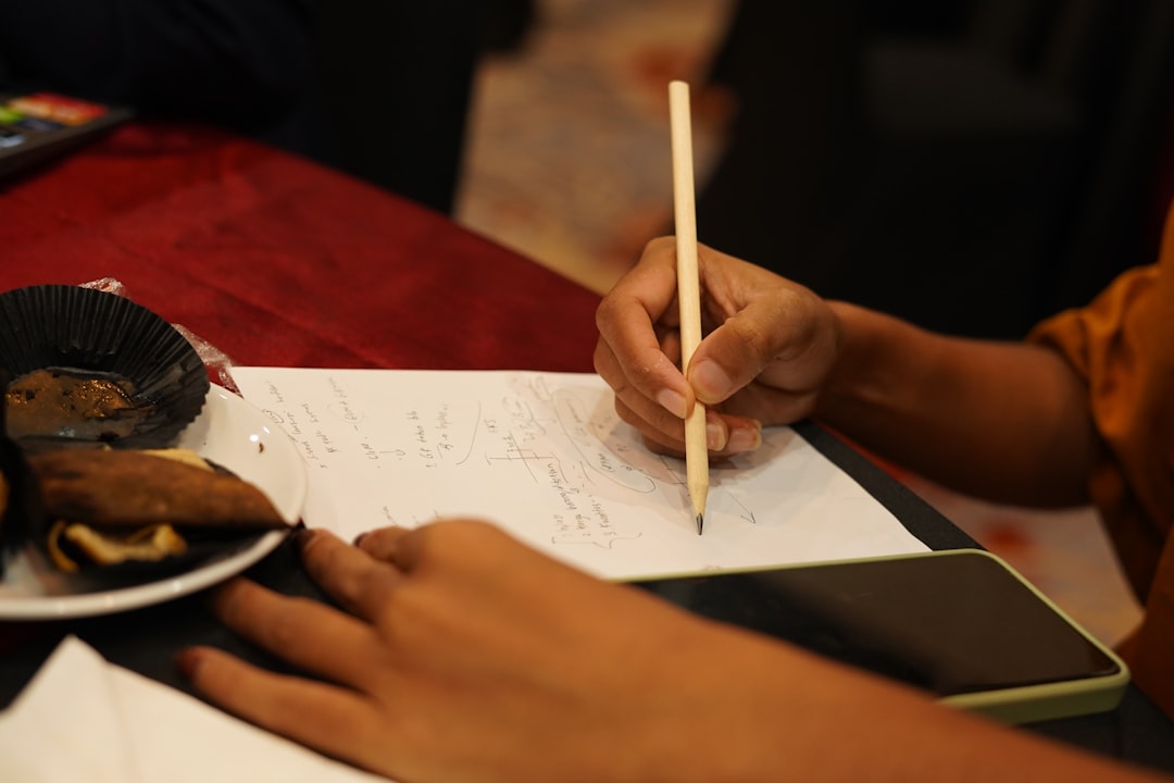 Close-up of compassionate teacher's hands guiding student's pencil work, warm golden hour lighting, blurred neural network visualization overlay, clean modern office setting, human connection emphasis