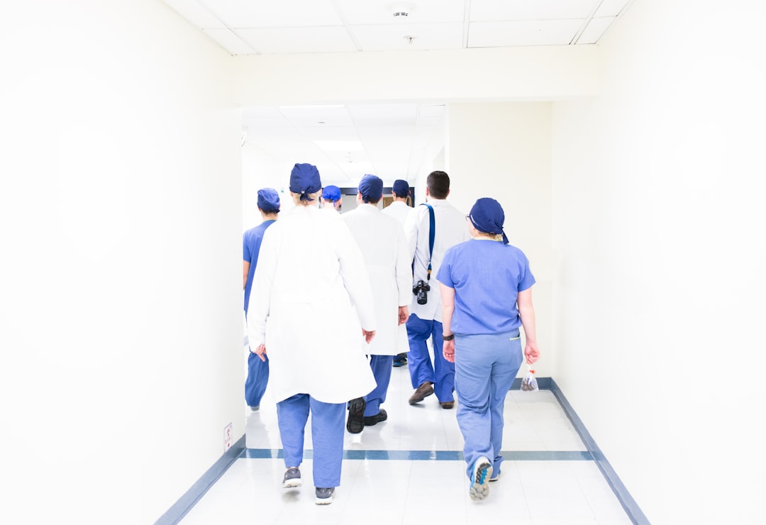 Diverse team of medical professionals and engineers examining floating regulatory compliance hologram with AI algorithm audit trail, warm amber server room lighting, glass walls with data center visib