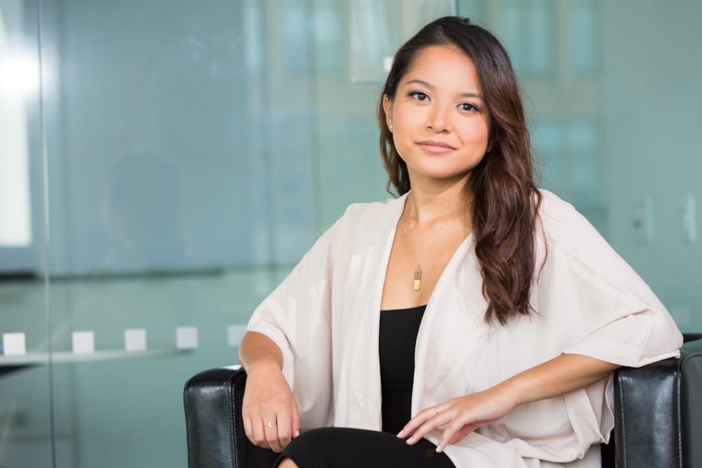 Young Gen Z professional woman facing holographic AI interface in sleek glass office, neon blue ambient lighting, human-machine interaction, futuristic corporate setting, cinematic depth of field
