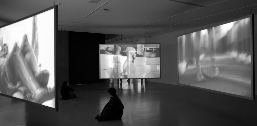 Futuristic museum gallery with holographic AI art installation, visitor silhouettes interacting with glowing neural network projections, sleek ambient lighting, clean modern architecture blending scie