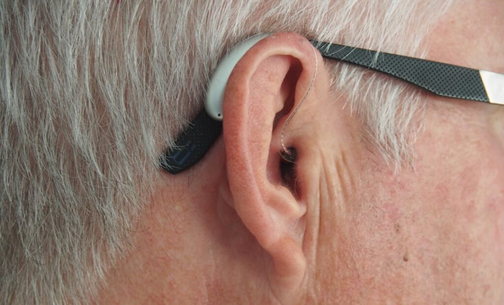 Futuristic close-up of human ear with holographic sound waves and neural network visualization, ambient blue lighting, sleek tech interface overlay, spiritual meditation silhouette in background, prof