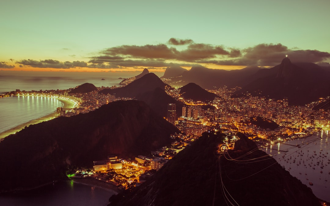 Futuristic cityscape of Rio de Janeiro at twilight with holographic data overlays, professional architect examining neural network visualization on transparent screen, sleek ambient blue lighting, cle
