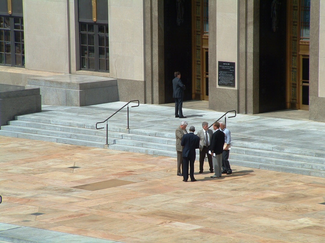 Diverse professionals in modern courthouse lobby examining transparent tablet with AI analytics, warm natural lighting, justice scales hologram, civic architecture, human-AI collaboration concept