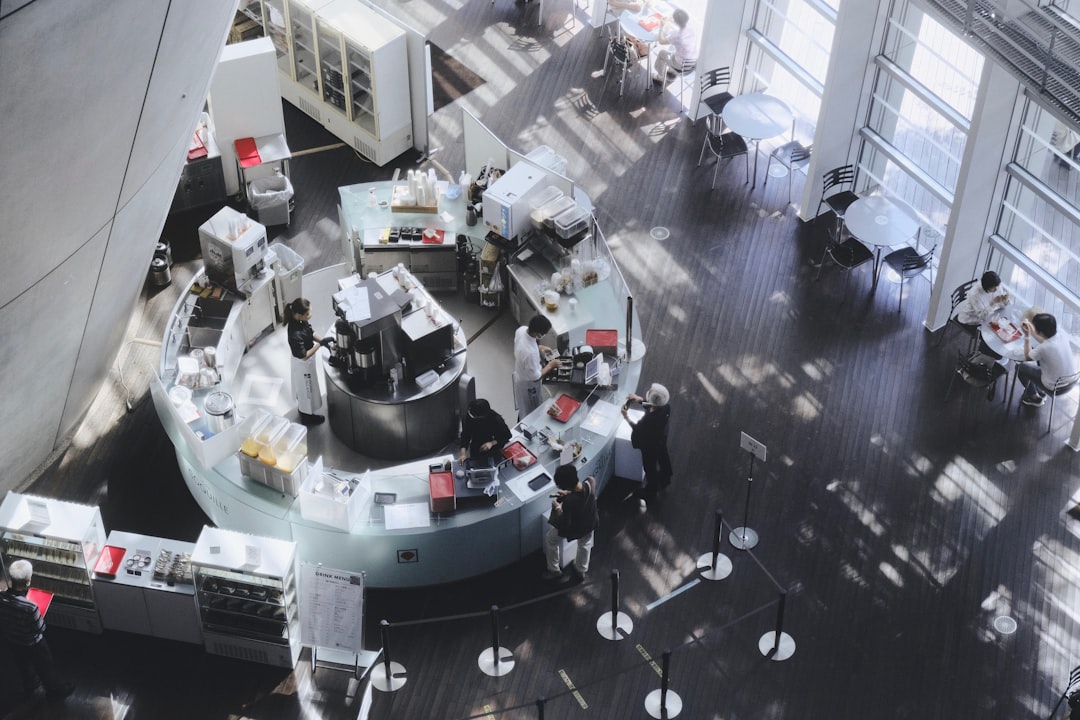 Aerial view of circular glass meeting room with holographic global data sphere, diverse team gesturing at floating interfaces, golden hour ambient light, collective intelligence visualization, archite