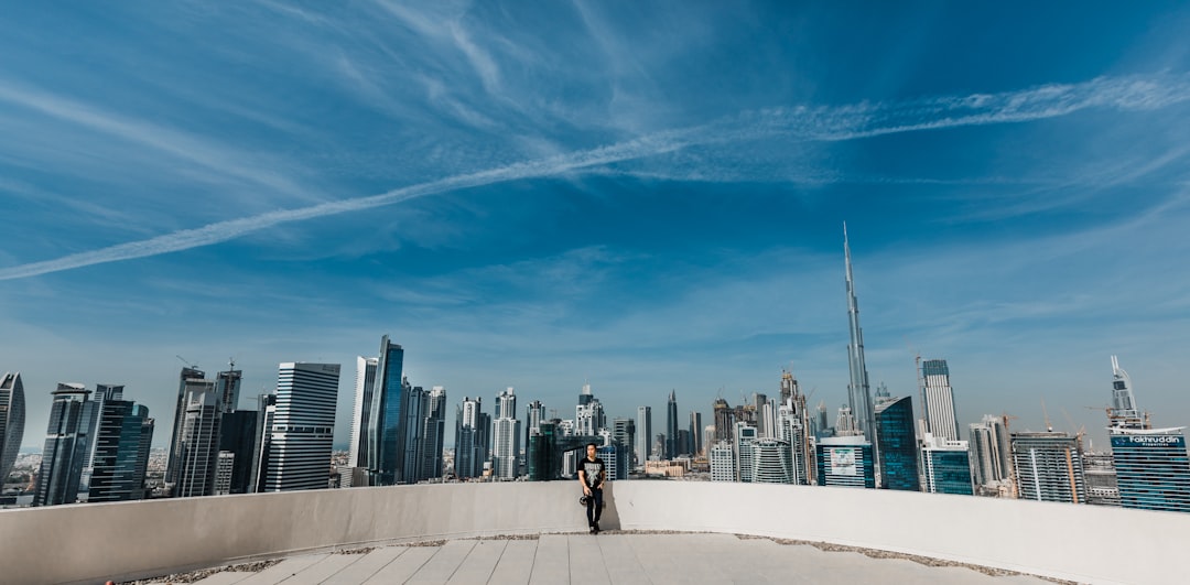 Middle Eastern professional woman interacting with holographic AI interface in modern Dubai tech hub with futuristic skyline visible through glass walls and warm golden ambient tones