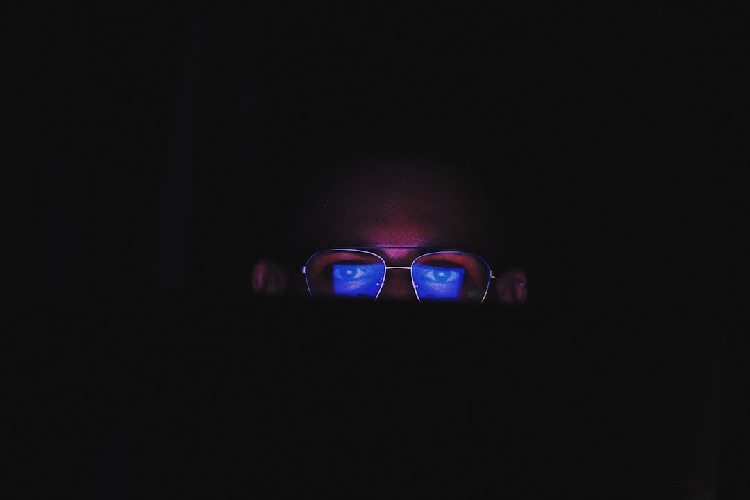 Close-up of sleek futuristic smart glasses with holographic display overlay, ambient blue lighting, clean modern tech lab, professional hands adjusting frame, neural network visualization reflected in