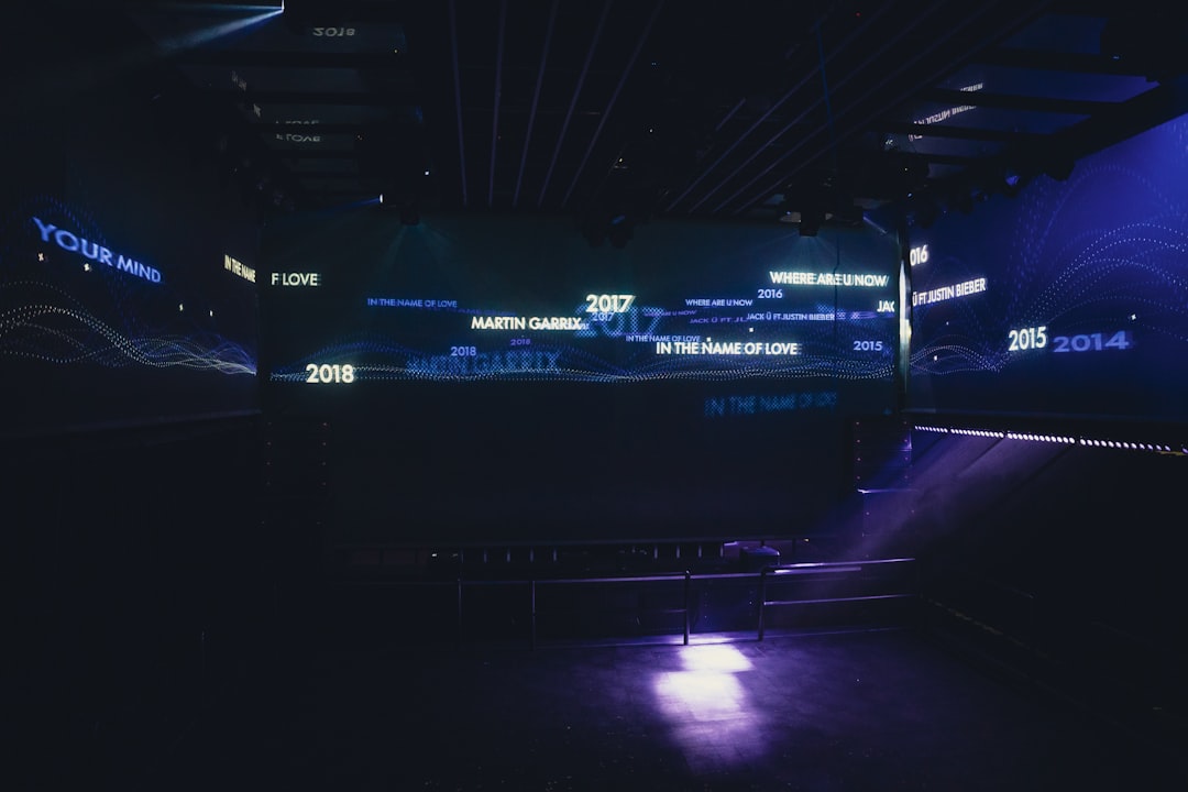 Aerial view of a packed futuristic stadium with massive holographic scoreboards and data streams, sleek commercial branding integration, golden hour lighting blending with cyan LED accents, profession
