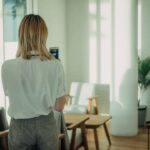 Professional woman in sleek clean modern office interacting with holographic display showing neural network visualization, futuristic ambient lighting blue tones, human-AI collaboration concept