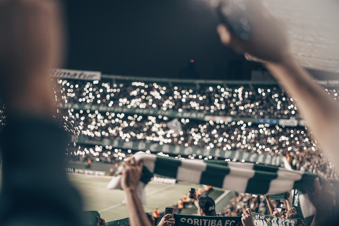 Excited diverse crowd of Brazilian soccer fans in stadium wearing augmented reality glasses seeing real-time player stats and heat maps overlaid on live match, vibrant energetic atmosphere, holographi