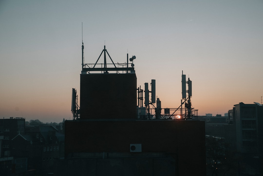 Sleek edge computing node installed on modern smart city rooftop at twilight, holographic data streams flowing to nearby buildings, professional technician with tablet monitoring decentralized network