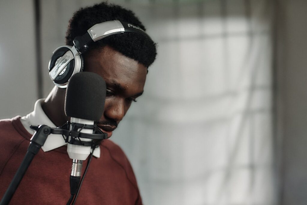 African music producer wearing sleek headphones interacts with holographic audio waveform display in futuristic Lagos studio, neon ambient lighting, data visualization overlays, professional tech envi