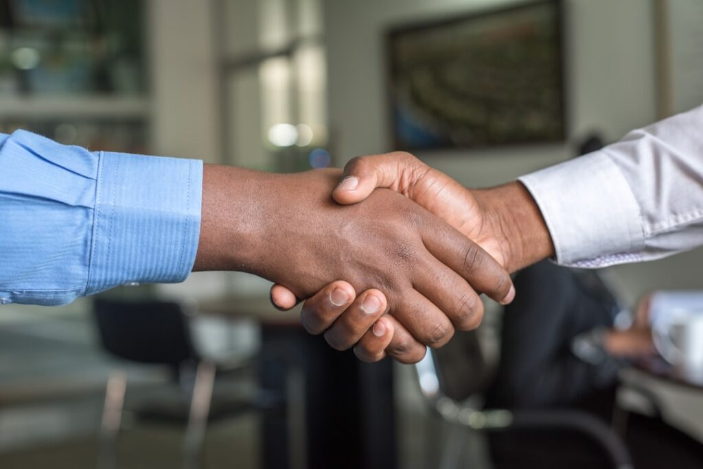 Two business professionals shaking hands in a futuristic server room with blue ambient lighting, holographic data visualizations, and rows of sleek GPU racks in background, corporate partnership conce