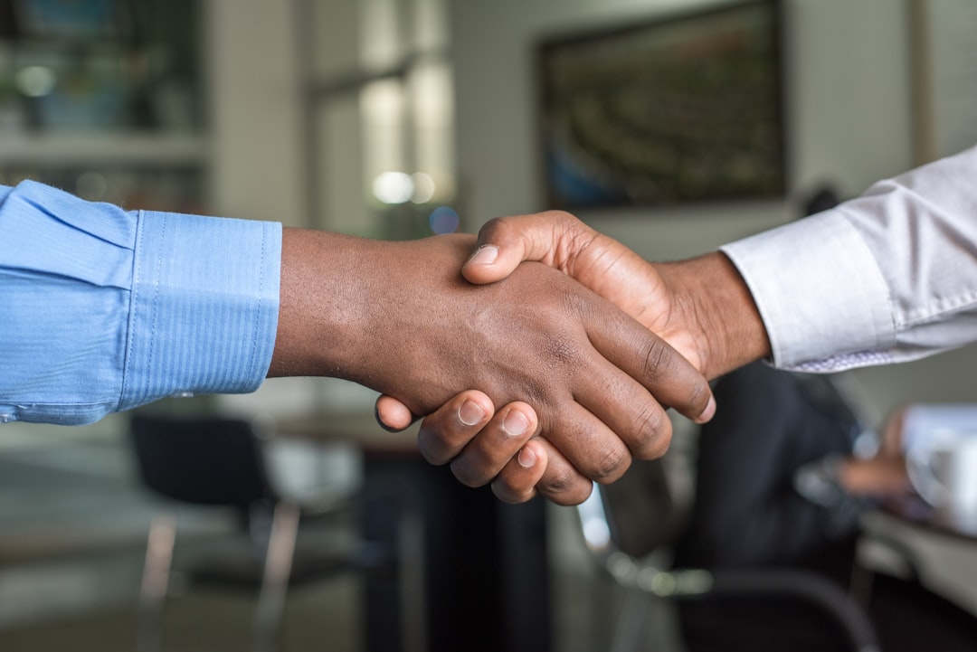 Two business professionals shaking hands in a futuristic server room with blue ambient lighting, holographic data visualizations, and rows of sleek GPU racks in background, corporate partnership conce