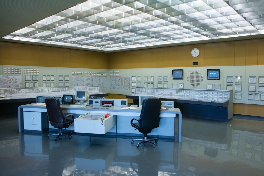Modern regulatory control room with curved glass displays showing compliance dashboards, diverse professionals collaborating, clean minimalist office, soft overhead lighting, holographic data streams