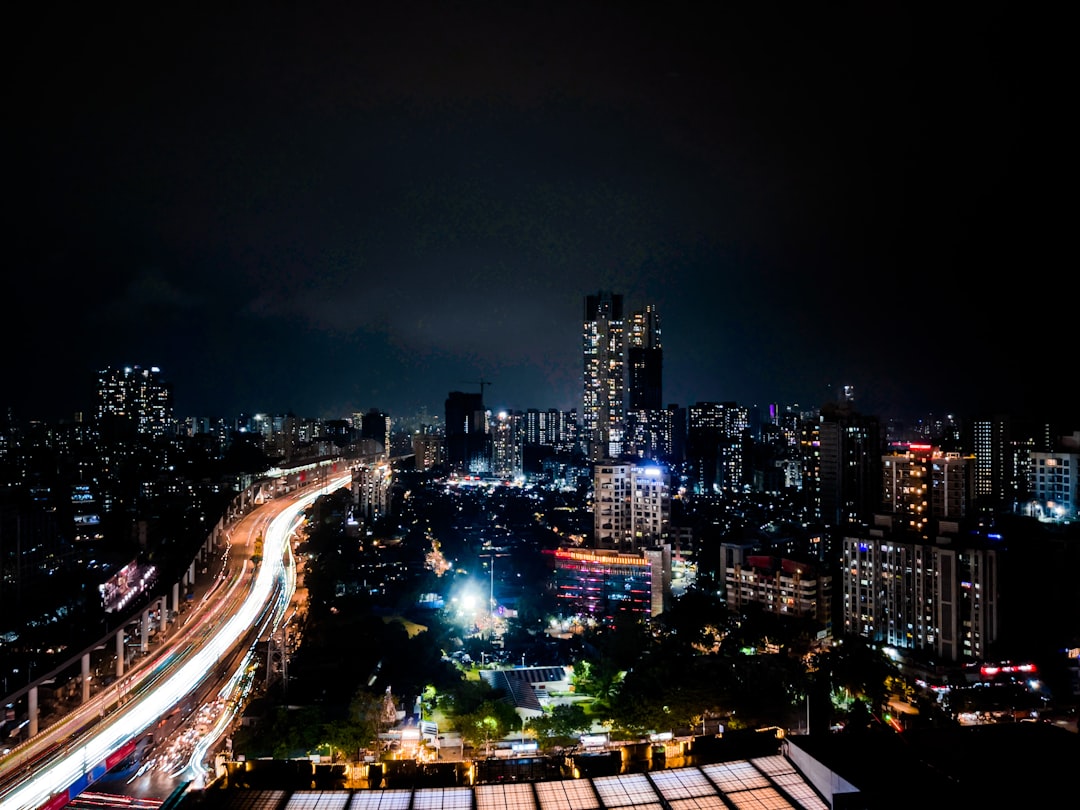 Wide angle of bustling Mumbai financial district at night with towering digital billboards showing stock charts and AI analytics, professional crowd below, sleek futuristic architecture, neon reflecti