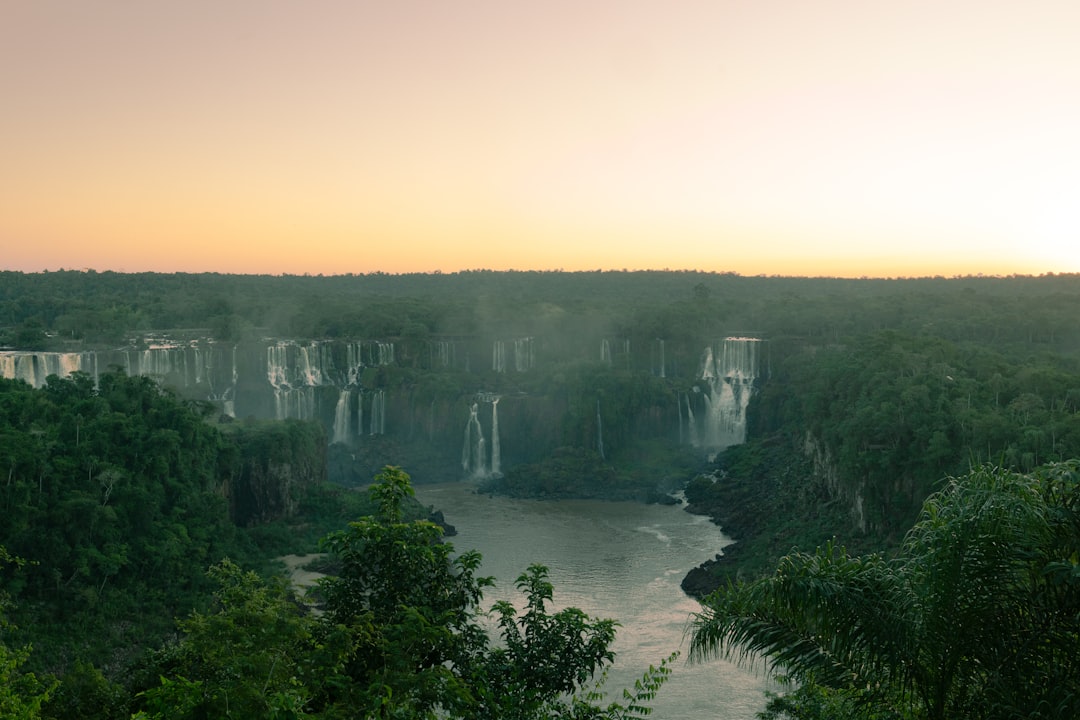 Futuristic aerial view of Foz do Iguacu waterfall at golden hour with holographic data overlays, diverse professionals in sleek conference setting, ambient teal and orange lighting, technology meets n