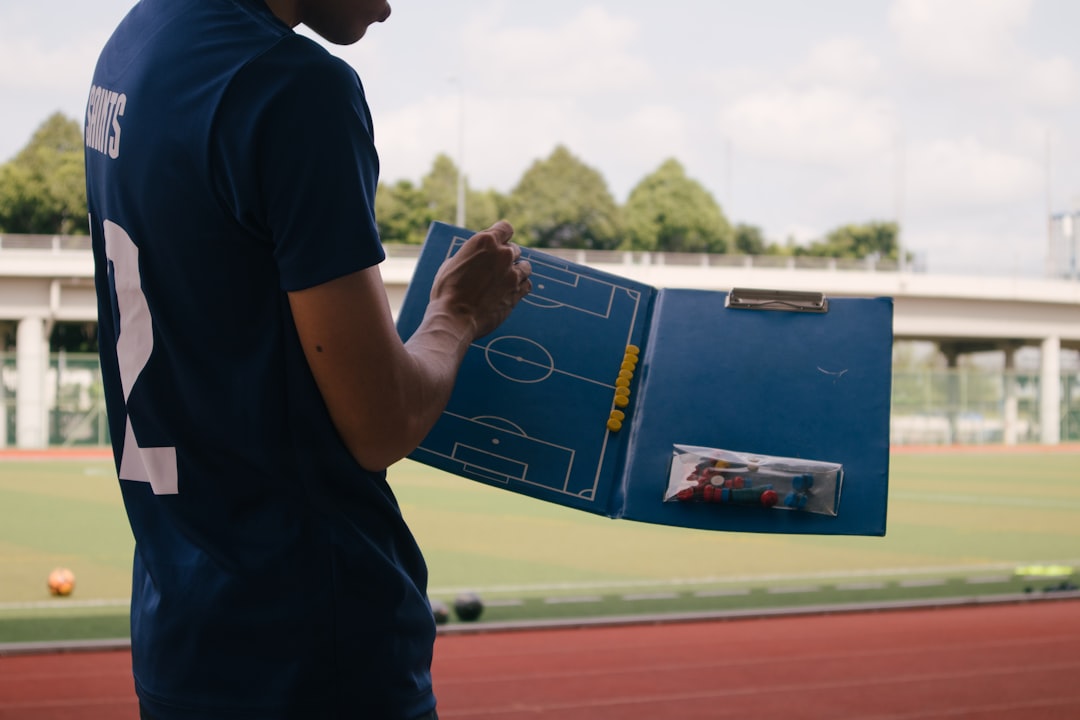Brazilian soccer coach reviewing futuristic touchscreen tactical board with real-time data streams in clean modern office with dramatic overhead lighting