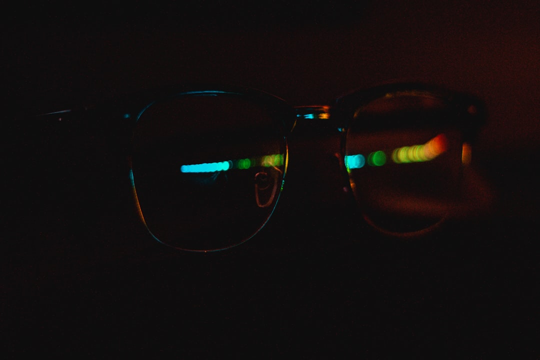 Close-up of sleek smart glasses lens reflecting neural network patterns, microchip circuitry glowing beneath, holographic facial mapping overlay, dark futuristic laboratory with purple ambient lightin
