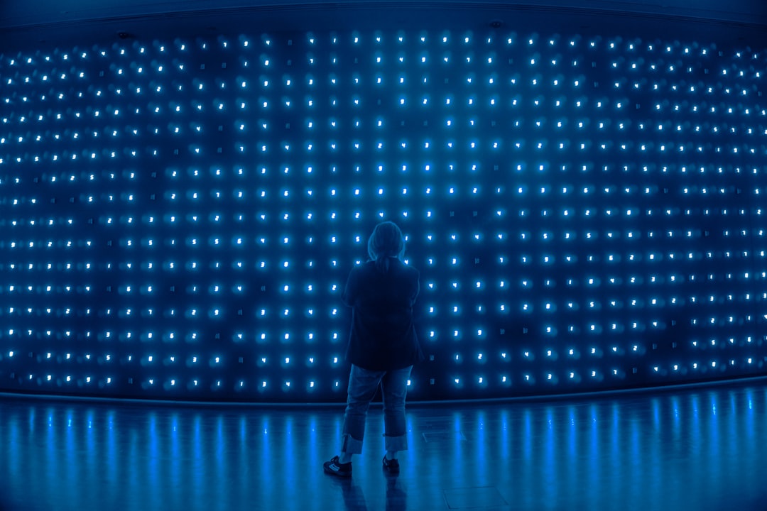 Futuristic data center with holographic LLM selection interface, professional analyst silhouette, blue ambient lighting, sleek server racks, neural network visualization floating in air, clean modern
