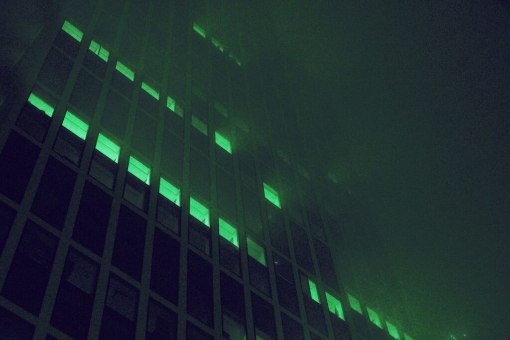 Crumbling corporate skyscraper hologram dissolving into digital particles, lone professional silhouette observing, dark moody ambient lighting, futuristic data center backdrop, teal and orange color g