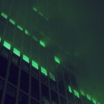 Crumbling corporate skyscraper hologram dissolving into digital particles, lone professional silhouette observing, dark moody ambient lighting, futuristic data center backdrop, teal and orange color g