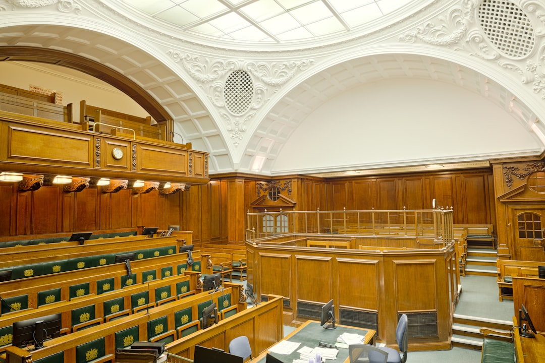 Dramatic courtroom interior with floating digital evidence holograms, professional judge's bench illuminated by cool white ambient light, AI ethics concept visualization with red warning nodes, sleek
